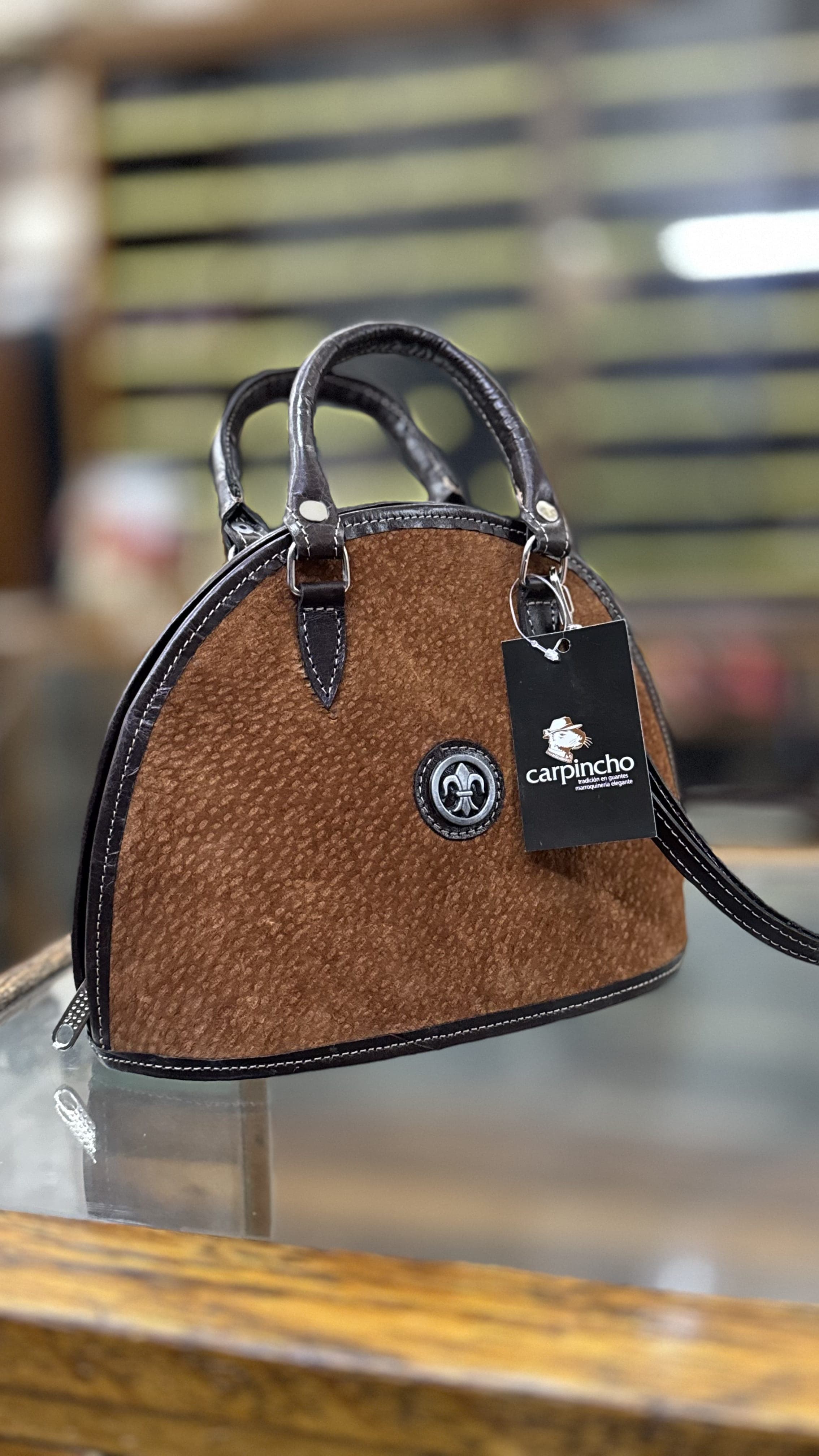 Cartera de carpincho marrón con vivos de cuero negro, sobre el mostrador del local de Casa Carpincho