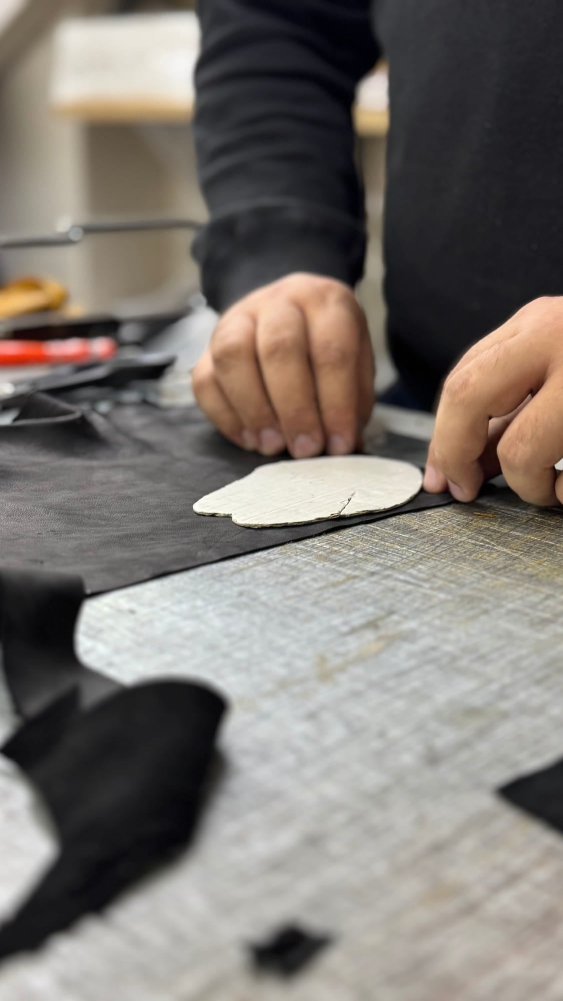 Manos apoyando el molde sobre una piel en la mesa de corte del taller